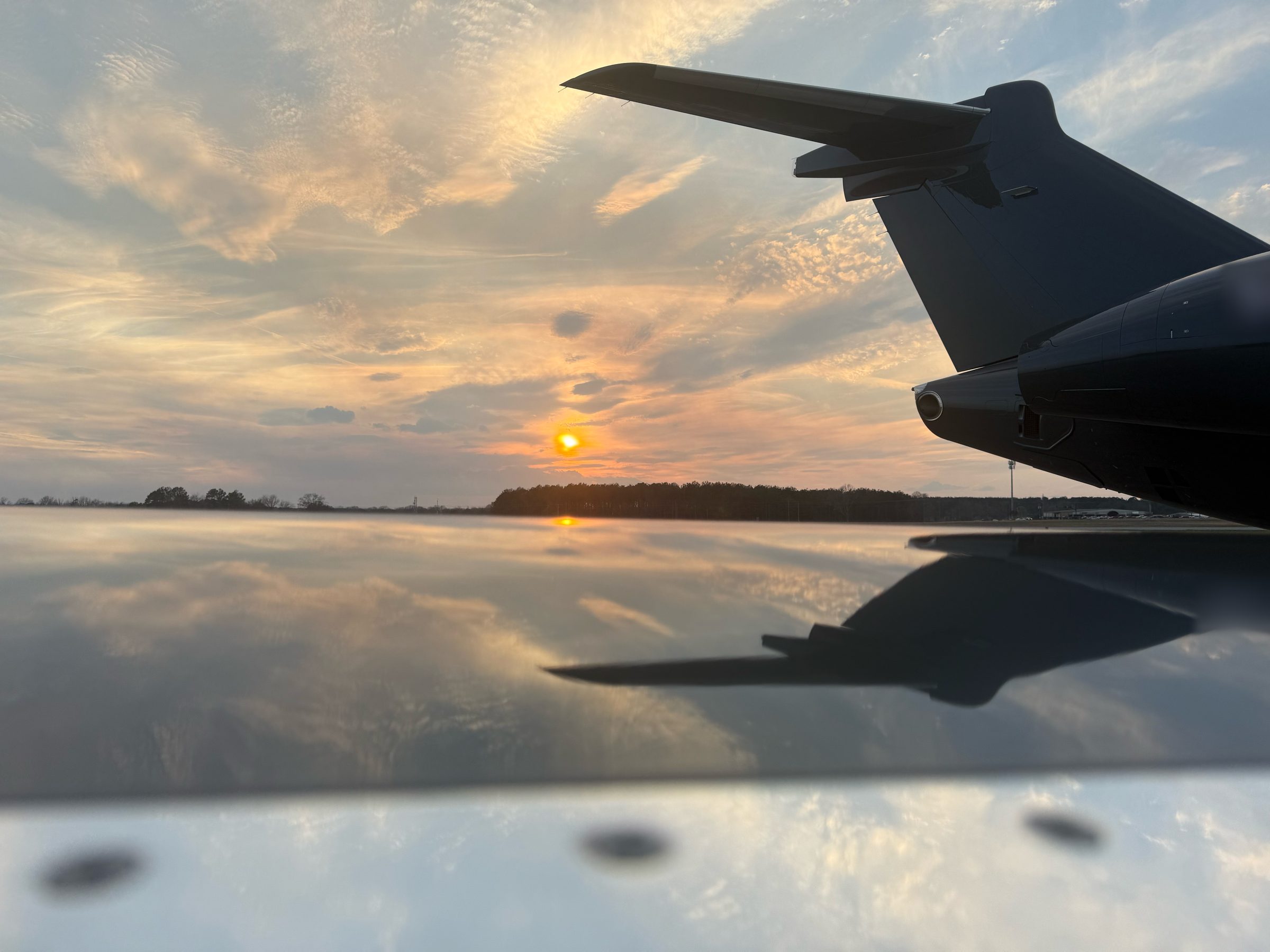 Business jet tail silhouetted against a sunset sky, reflected in a polished wing