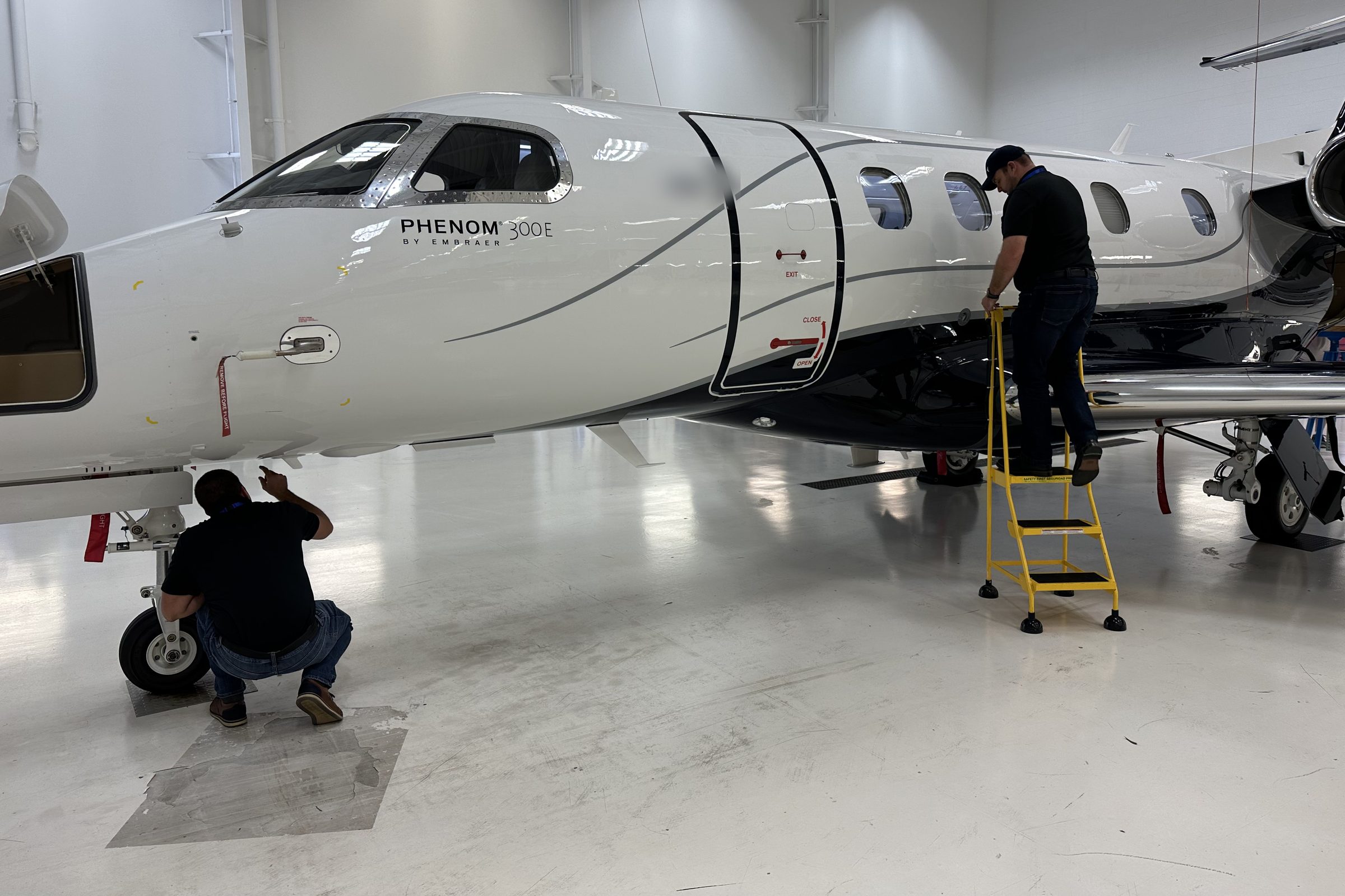 Technicians inspecting a new Phenom 300E in a hangar before delivery